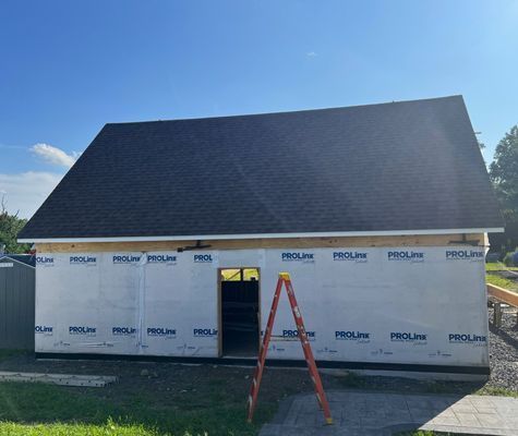 A new building with black roof and open door; construction in progress, an orange ladder.