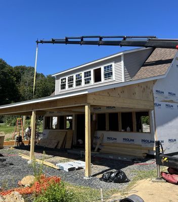Construction of a house with a porch, crane overhead, clear blue sky, sunny day.