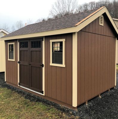 Brown shed with beige trim, doors, windows, and a brown roof. Located outdoors.