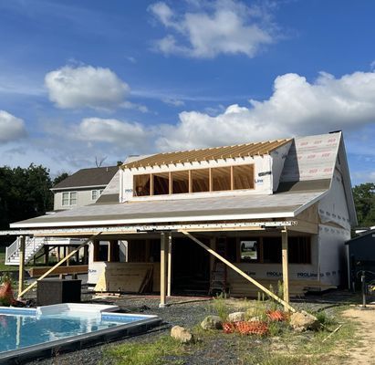 Construction of a wood-framed house with a pool, blue sky, and clouds.