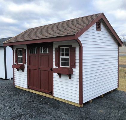 White storage shed with brown trim, doors, shutters, and roof, on gravel.