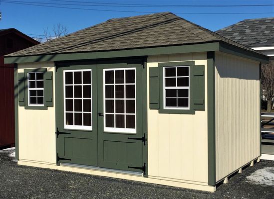 Light beige shed with green trim, double doors, windows, and shutters.