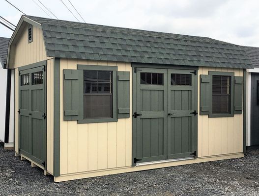 Tan and green shed with a green roof, double doors, and shuttered windows.