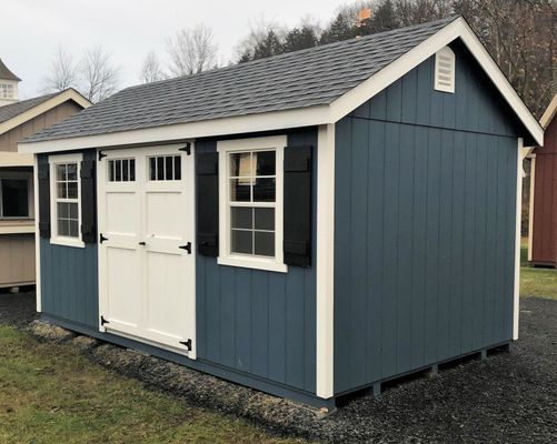 Blue storage shed with white trim and doors, black shutters, and a gray roof.