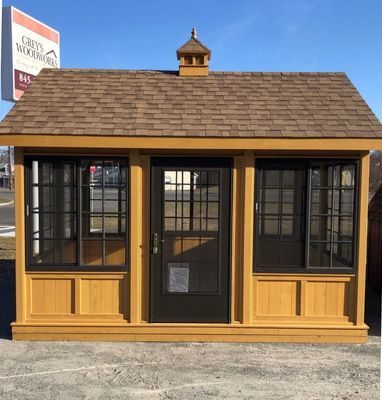 Wooden shed with brown roof, black windows and door, and tan siding, outdoors.