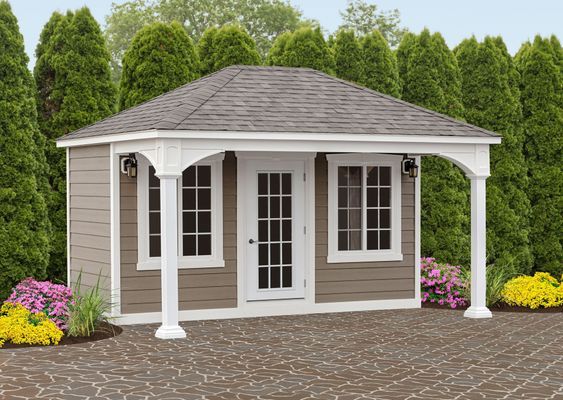 Brown and white shed with porch, double doors, windows, and flowers in front.