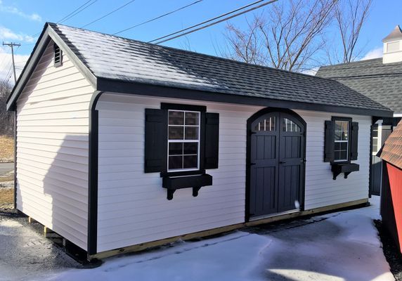 White shed with black trim, door, and shutters; snow on the roof and ground.