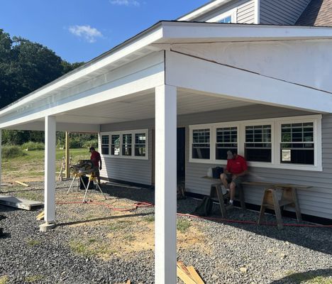 Two construction workers building a gray house with white trim and a covered porch.