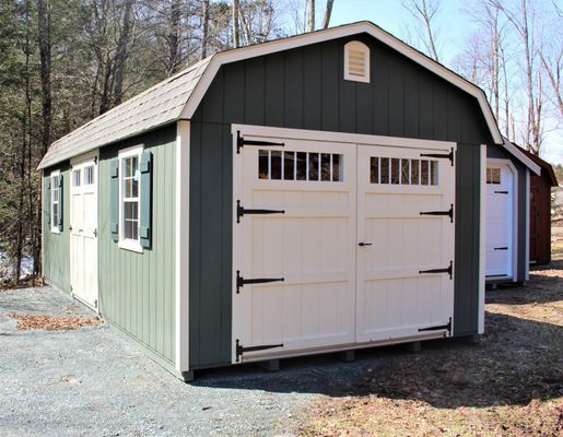 Green and white barn-style shed with white double doors, windows, and a gray roof; set outdoors.