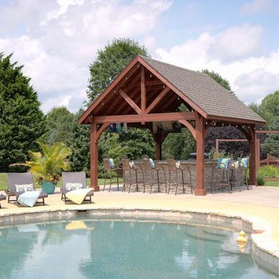Poolside gazebo with bar and seating. Brown wood structure and roof, pool in the foreground.
