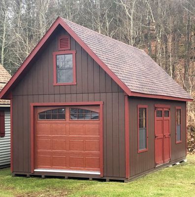Brown shed with red trim, garage door, double doors, and a small window, set in a yard.