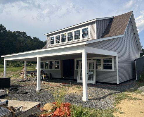 New house under construction with gray siding, white trim, and a covered porch.