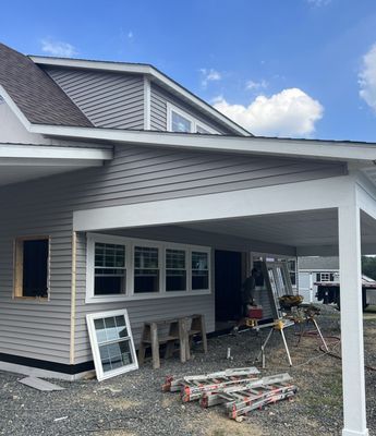 New house construction with gray siding, white trim, and a carport under a cloudy sky.