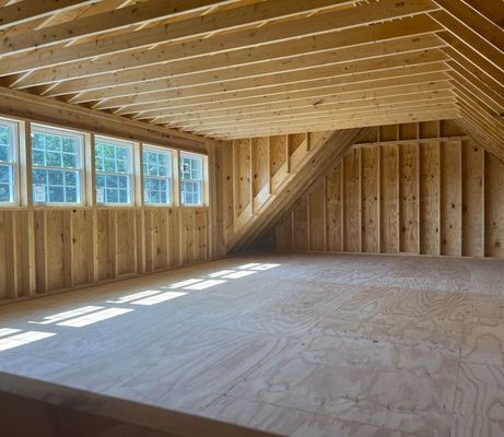 Interior of unfinished wooden attic with windows and sloped ceiling.