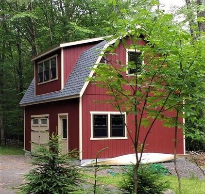 Red two-story barn-style building with a gray roof, surrounded by trees.