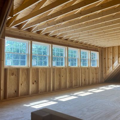 Interior view of a wooden framed room with several windows along the wall. Sunlight streams in.