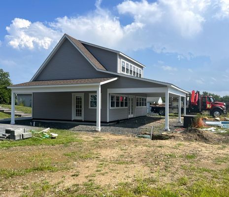 Two-story house with gray siding, covered porch, white posts, and a construction site in the background.