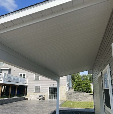 A carport attached to a gray house with white trim, on a sunny day.