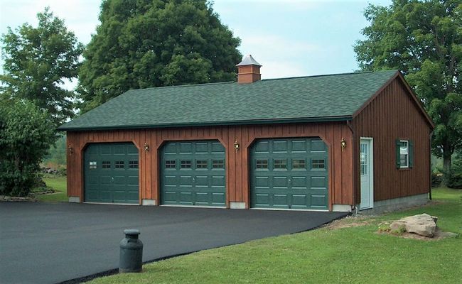 Three-bay garage with green doors and a brown exterior; on a paved driveway.