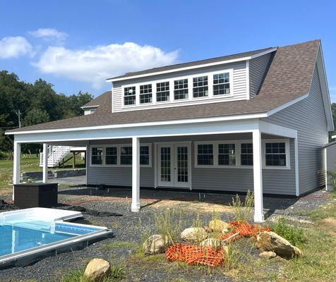 Gray-sided house with a covered patio, windows, and a pool in an outdoor setting.