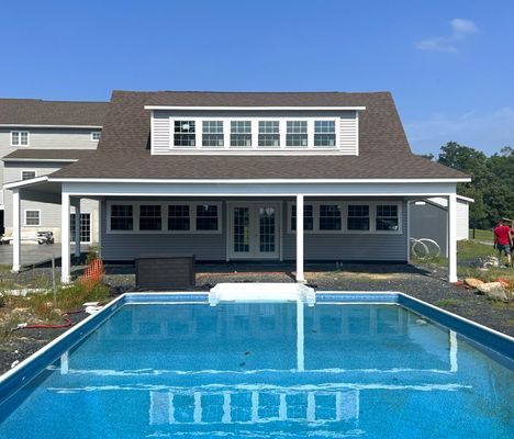 A backyard with a pool and gray house with a covered patio; sunny day.