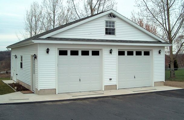 White two-car garage with gable roof, window, and light fixtures on a concrete slab; asphalt driveway.