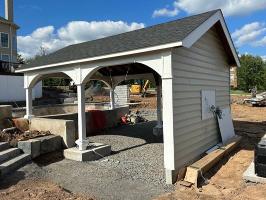 A light-colored shed with arched openings, under construction, on a gravel foundation.