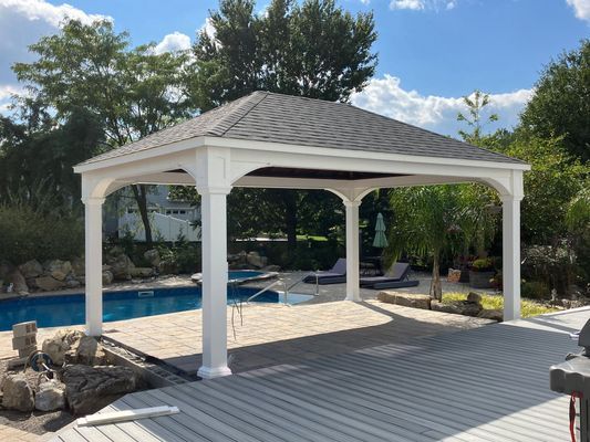White gazebo with dark roof over a wooden deck near a pool.