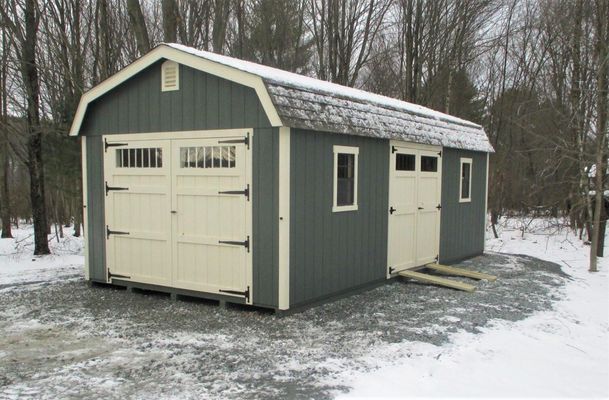 A blue-green barn-style shed with beige doors, snow on the ground, and a small ramp.