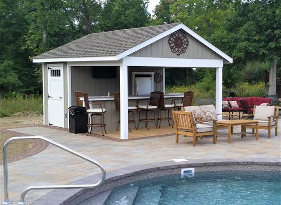 Poolside outdoor bar with seating, refrigerator, TV, and decorative wall art; gray and white.
