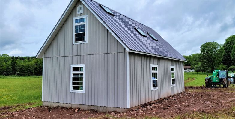 Gray barn with metal roof, windows, and a tractor in a field.