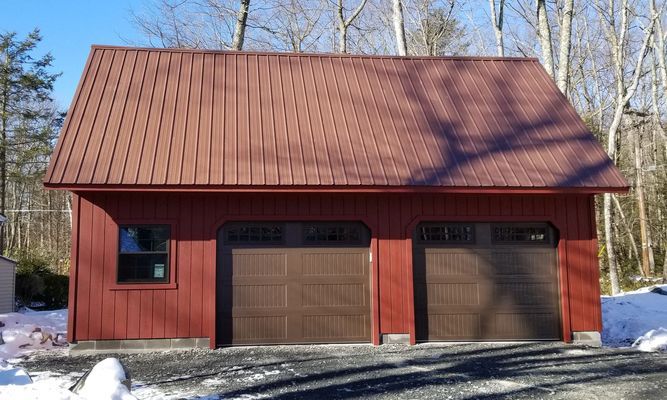 Red garage with brown doors and roof, a window, set in a snowy outdoor area.