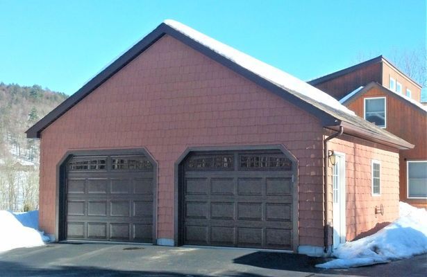 Two-car garage with brown doors and reddish-brown siding, roof has some snow. Sunny day.