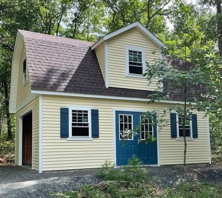 Two-story yellow building with a dark roof and blue accents, in a wooded setting.