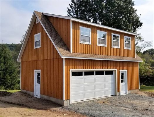 Two-story wooden garage with tan siding and white doors and trim.