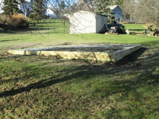 Rectangular concrete foundation in a grassy yard, with a small shed in the background.
