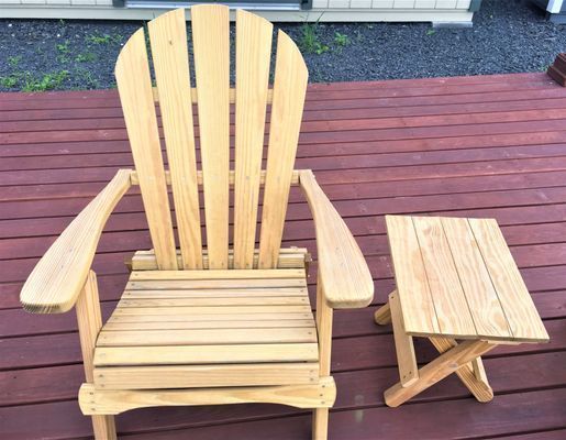 Wooden Adirondack chair and small side table on a red-brown deck.