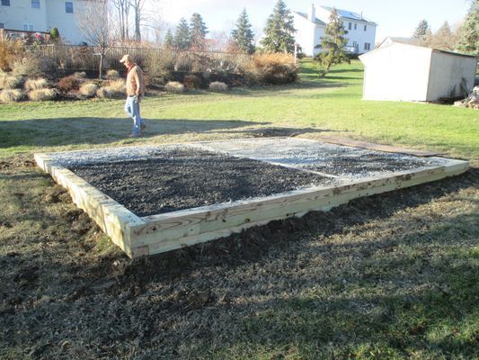 A raised garden bed constructed of wood, filled with dark soil, in a grassy yard. A person stands nearby.