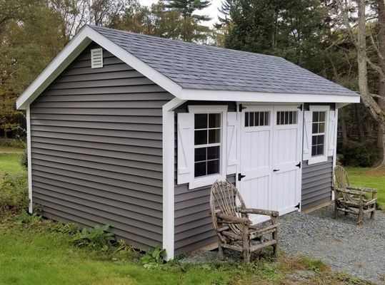Gray-sided shed with white trim, doors, and shutters. Includes lawn chairs and gravel path.