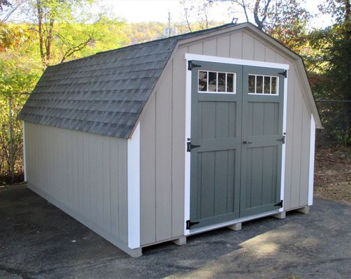Tan shed with green doors, white trim, and a gray roof, sitting outdoors.
