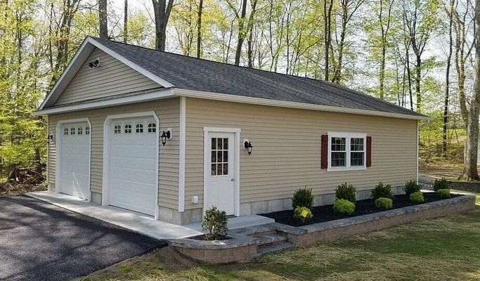 Tan garage with two bays, white doors, and a side entrance; landscaping in front.