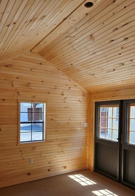 Wooden-walled interior with sloped ceiling. Window and double doors let in sunlight.