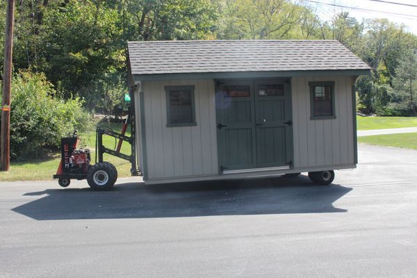 A small shed being towed down a road by a red tractor. The shed is light green with a dark green door.