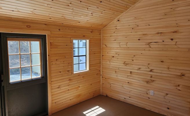 Interior of a small wooden cabin with a door and window letting in sunlight.