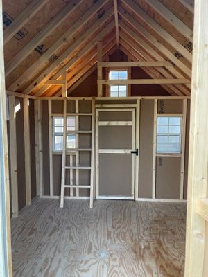 Inside of a wooden shed under construction, featuring a door, windows, and a ladder.