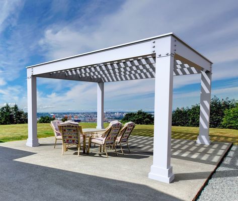 White pergola over outdoor dining set on a concrete patio, overlooking a city and blue sky.
