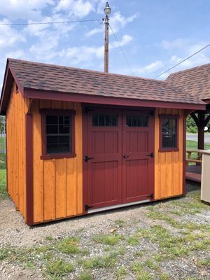 Orange and red wooden shed with double doors and windows, brown roof, sitting on grass.