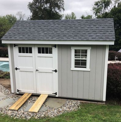 Gray shed with white doors, ramp, and small window. Exterior on a grassy area.