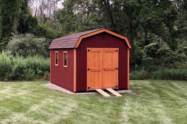 Red shed with white trim and brown roof, gravel base, wooden ramps.