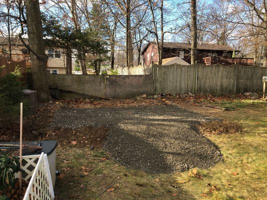 Gravel path in a backyard, near a wooden fence and trees, on a sunny day.